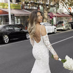 Elegant fitted wedding dress with floral appliqué sleeves and backless design, bride holding white bouquet on city street — You&I Bridal | Endless UAE
