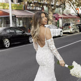 Elegant fitted wedding dress with floral appliqué sleeves and backless design, bride holding white bouquet on city street — You&I Bridal | Endless UAE