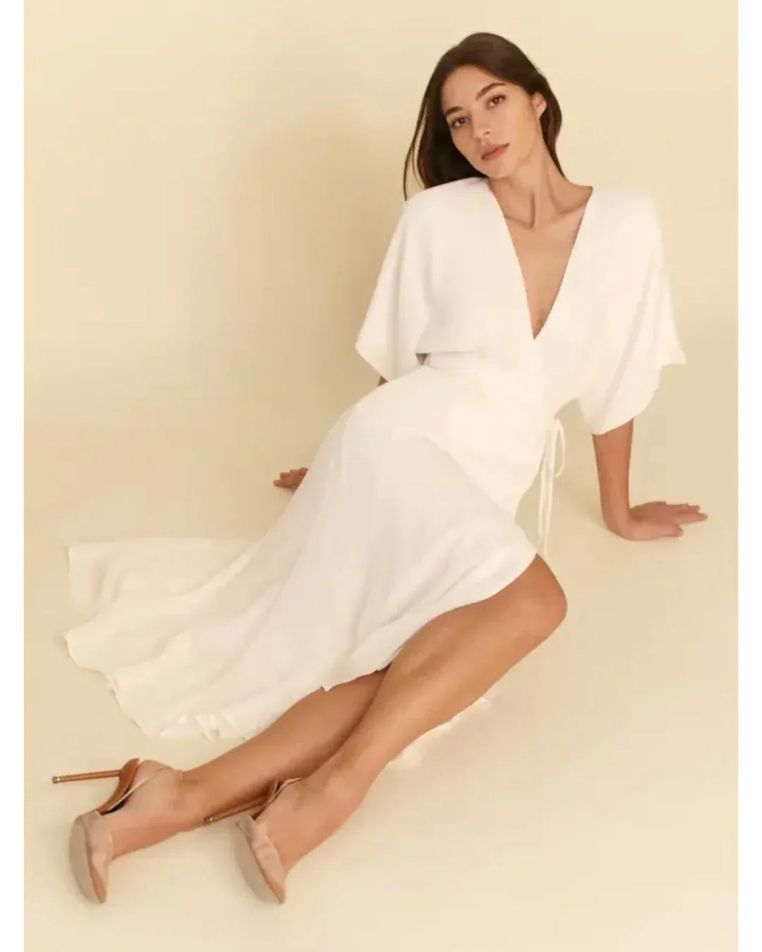 Woman sitting wearing white midi dress with V-neck and flutter sleeves paired with beige heels — Reformation | Endless UAE