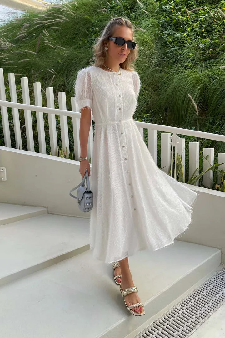 Woman wearing white sequin button-front midi dress with sheer sleeves and gold sandals on outdoor steps — Post Meridiem | Endless UAE