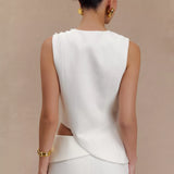 Rear view of woman wearing white sleeveless asymmetric suiting top with gold jewelry and hair in bun — Endless | Endless UAE