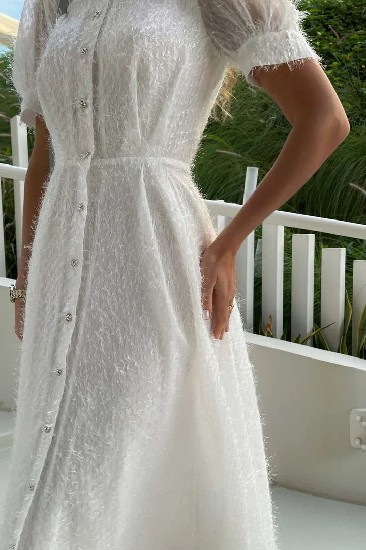 Woman wearing white textured midi dress with sequin button front and short sleeves on outdoor terrace — Post Meridiem | Endless UAE