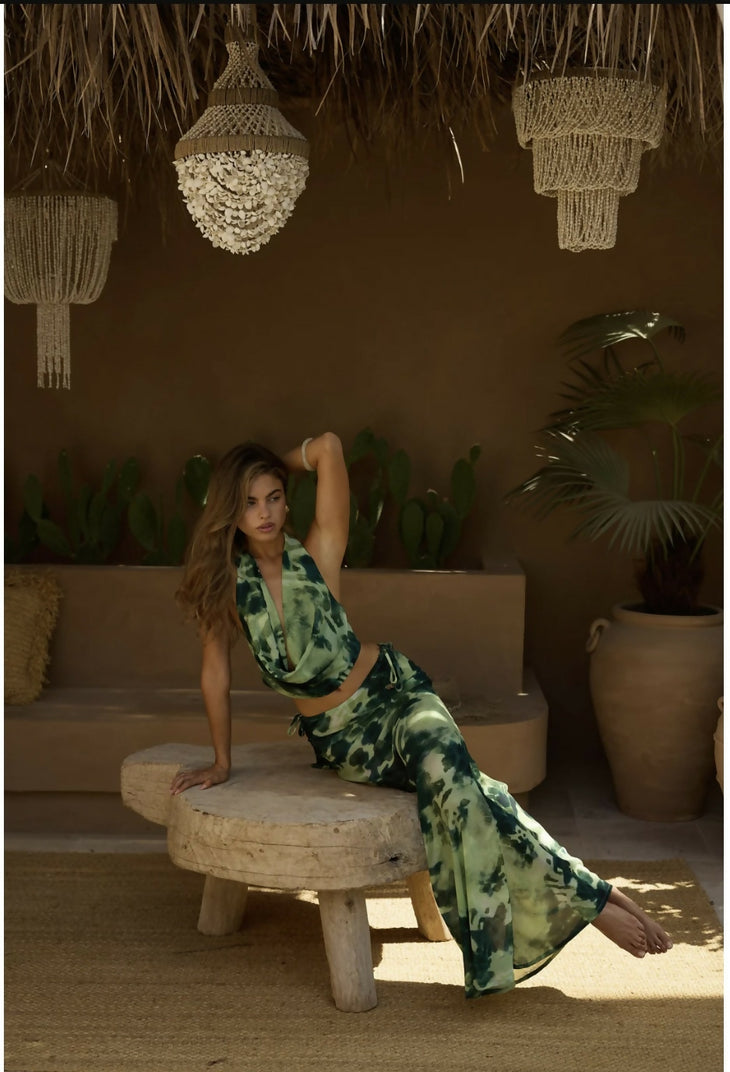 Woman wearing green tie-dye maxi skirt in tropical bohemian setting with hanging shell chandeliers — Beach City | Endless UAE