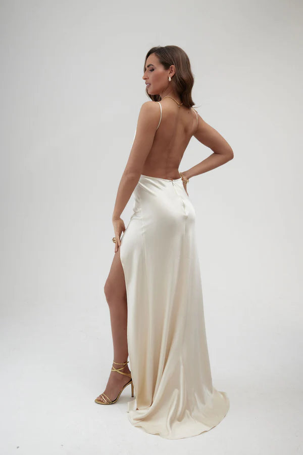 Elegant ivory satin backless maxi dress with high slit and thin straps, worn with gold strappy heels — By Keara | Endless UAE