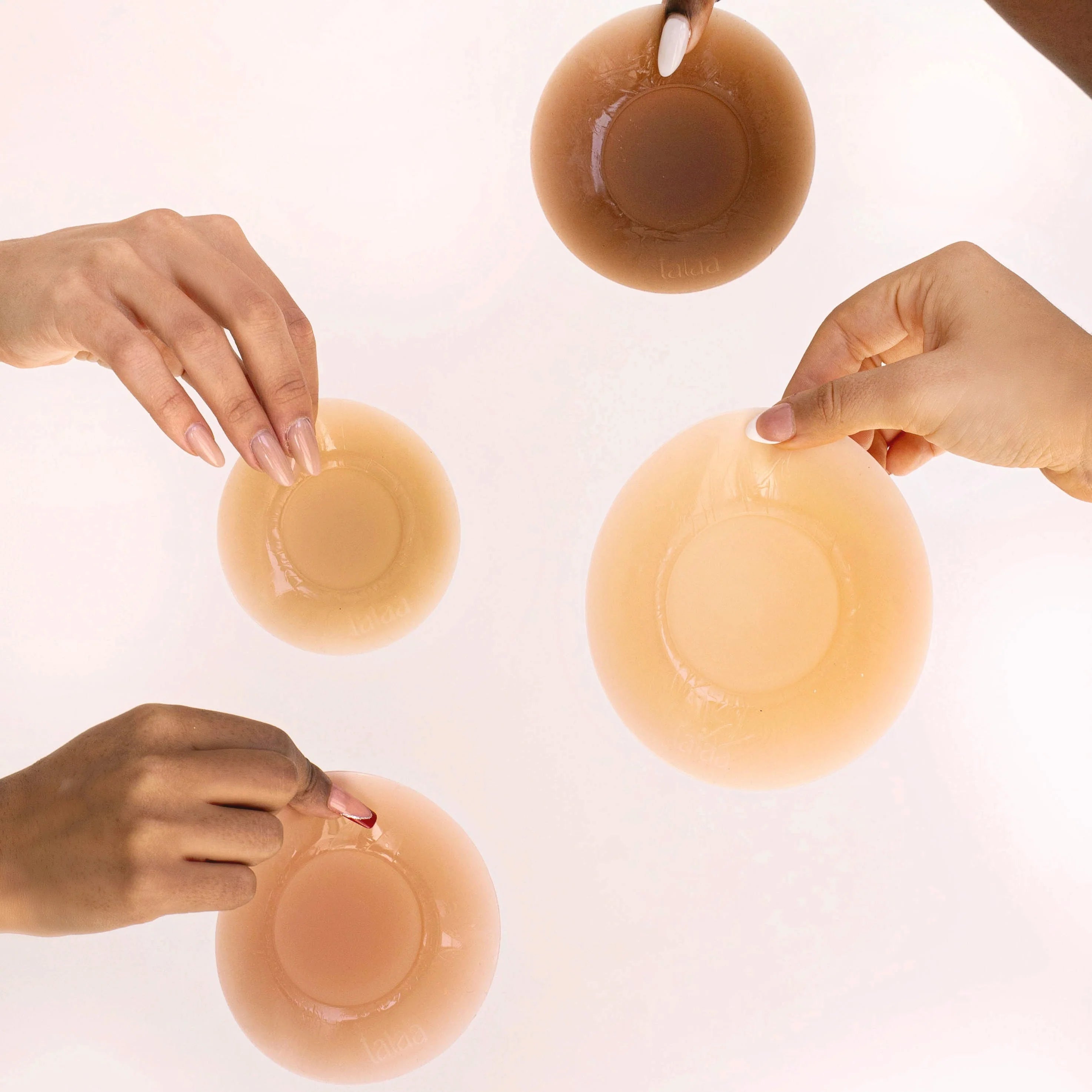 Four hands holding nude-toned reusable silicone nipple covers in various skin shades on white background — Talaa | Endless UAE