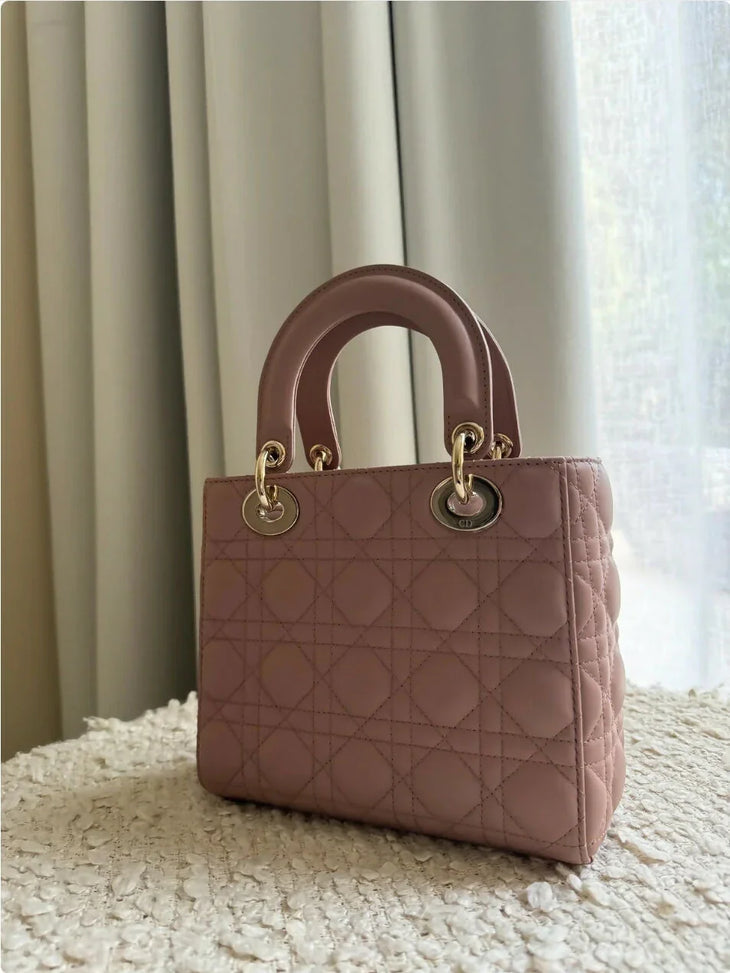 Small mauve quilted Lady Dior bag with gold hardware and rounded top handles on white textured surface — Christian Dior | Endless UAE