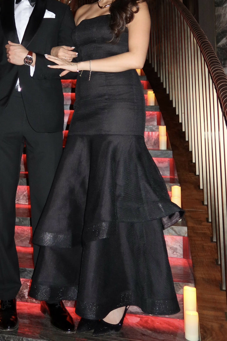 Elegant black strapless midi dress with tiered ruffle skirt and textured fabric, photographed on stairs with decorative lighting — Coast | Endless UAE