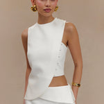 Woman wearing white sleeveless asymmetric top with side cutout detail and gold button accents, styled with gold jewelry — Endless | Endless UAE
