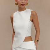 Woman wearing white sleeveless asymmetric top with side cutout detail and gold button accents, styled with gold jewelry — Endless | Endless UAE