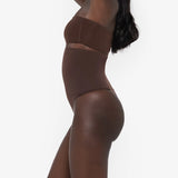 Woman wearing beige high waist thong in standing pose — Underhance | Endless UAE