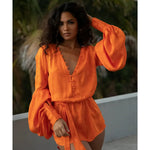 Woman wearing vibrant orange flowing mini dress with long sleeves and tie waist by poolside — Rat & Boa | Endless UAE