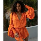 Woman wearing vibrant orange flowing mini dress with long sleeves and tie waist by poolside — Rat & Boa | Endless UAE