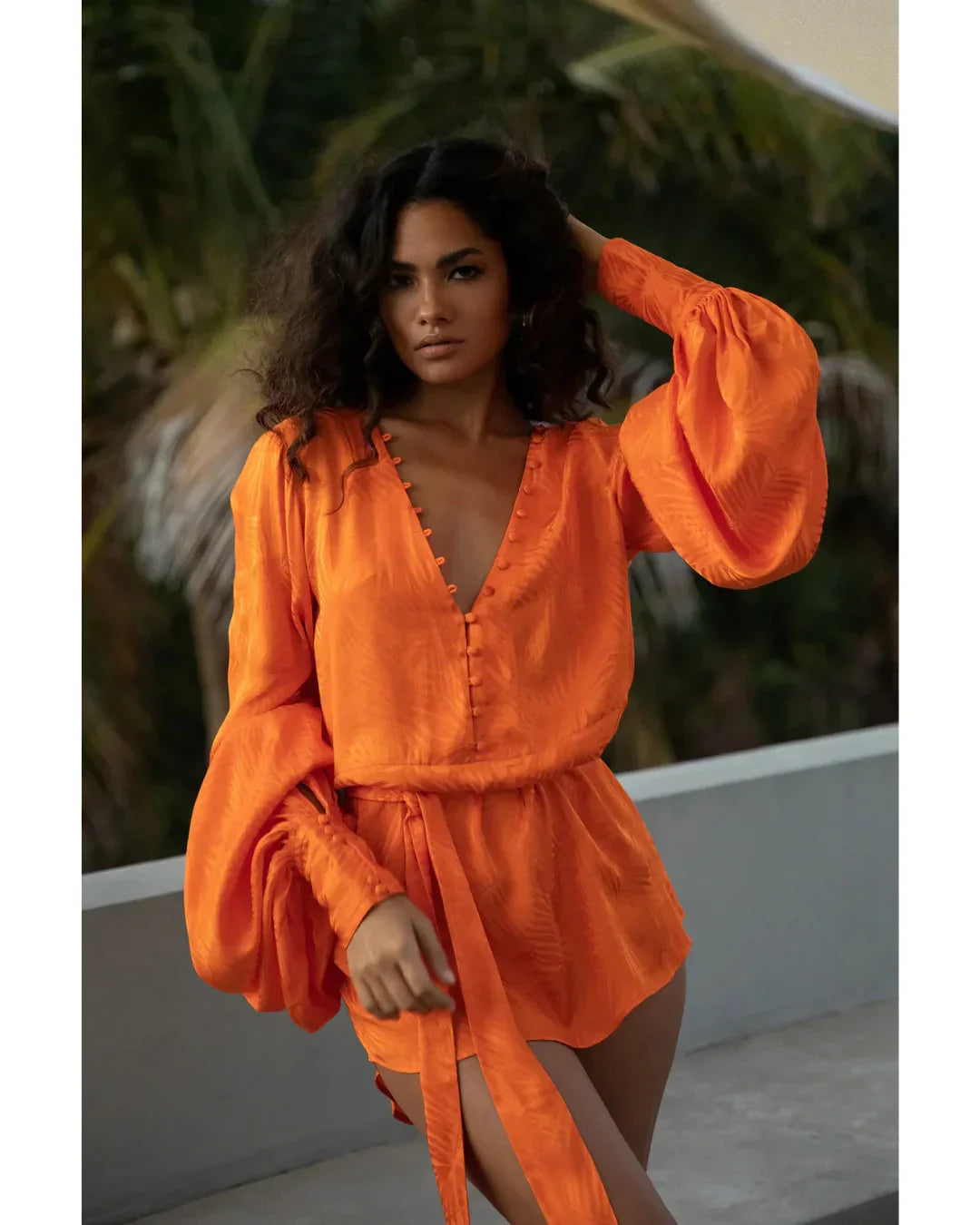 Woman wearing vibrant orange flowing mini dress with long sleeves and tie waist by poolside — Rat & Boa | Endless UAE