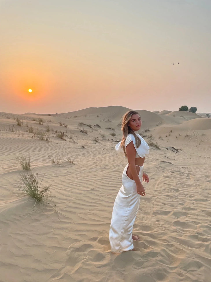Cream Faye Co-ord Set featuring draped crop top and maxi skirt on model in desert landscape — Deme Studio | Endless UAE