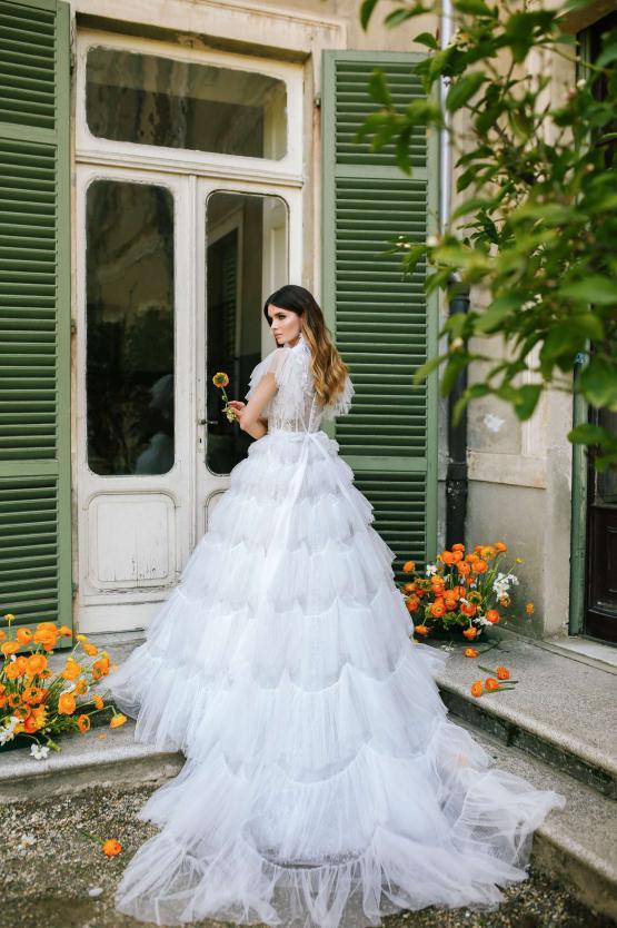 Bride in white tiered tulle Lorenso gown with floral accents at vintage green doorway — Blammo Biamo | Endless UAE