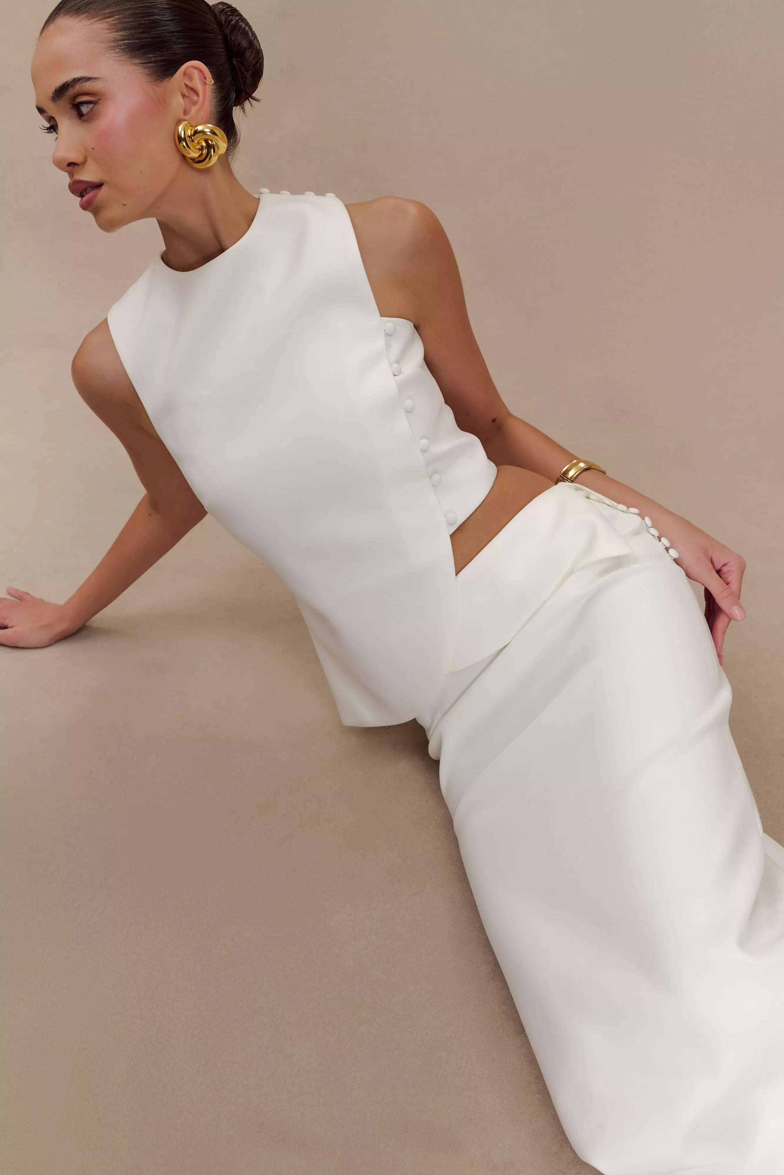Elegant white asymmetric sleeveless top with pearl button detail, styled with matching trousers and gold jewelry — Endless | Endless UAE