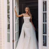 Bride in fitted lace wedding gown with illusion neckline and flowing tulle overskirt standing in white doorway — You&I Bridal | Endless UAE