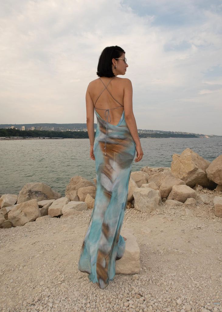Woman wearing blue tie-dye maxi dress standing on rocky beach — Dvete | Endless UAE