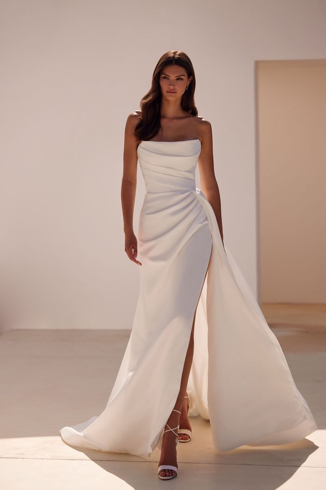 Elegant white strapless bridal gown with draped bodice and high slit, paired with strappy sandals — Milla Nova | Endless UAE