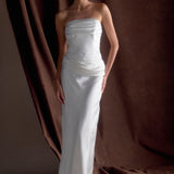 Woman wearing elegant white strapless satin maxi dress with ruched bodice detailing against brown curtain backdrop — Meshki | Endless UAE