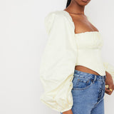 Pale yellow corset top with dramatic puff sleeves and square neckline paired with blue jeans — House of CB | Endless UAE