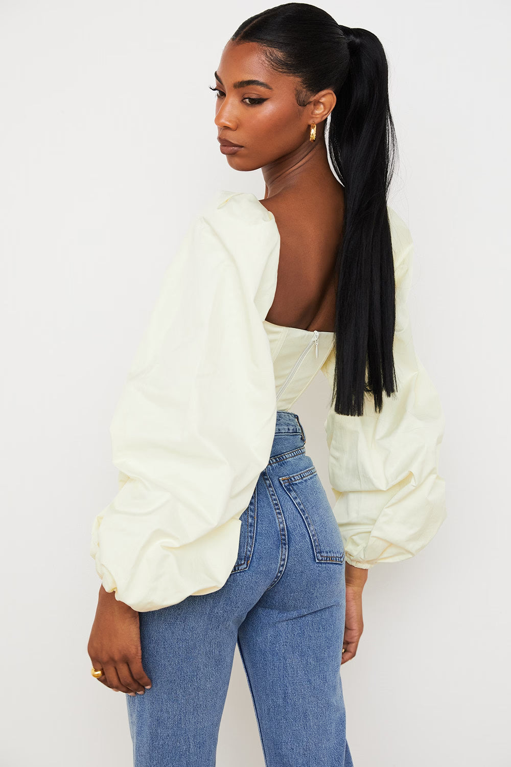 Woman wearing cream balloon sleeve corset top with blue jeans viewed from side — House of CB | Endless UAE