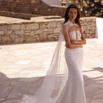 Elegant strapless mermaid wedding dress with embellished bodice and flowing cape in sunlit courtyard — You&I Bridal | Endless UAE