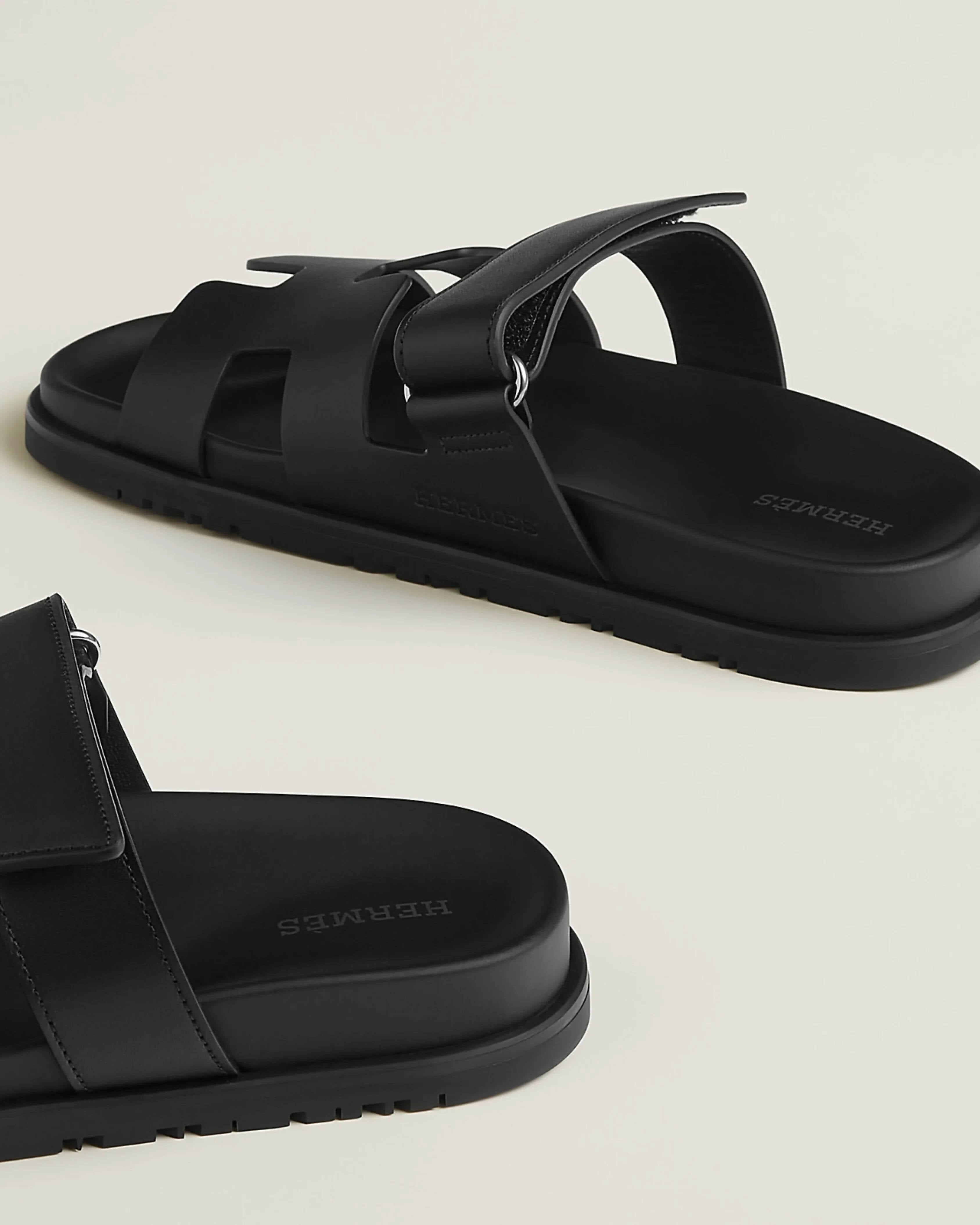 Black leather slide sandals with adjustable buckle straps and textured rubber sole — Hermes | Endless UAE