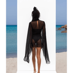 Black sheer mesh maxi dress with flowing cape sleeves and cutout back detail, worn by model at beach — Rat & Boa | Endless UAE