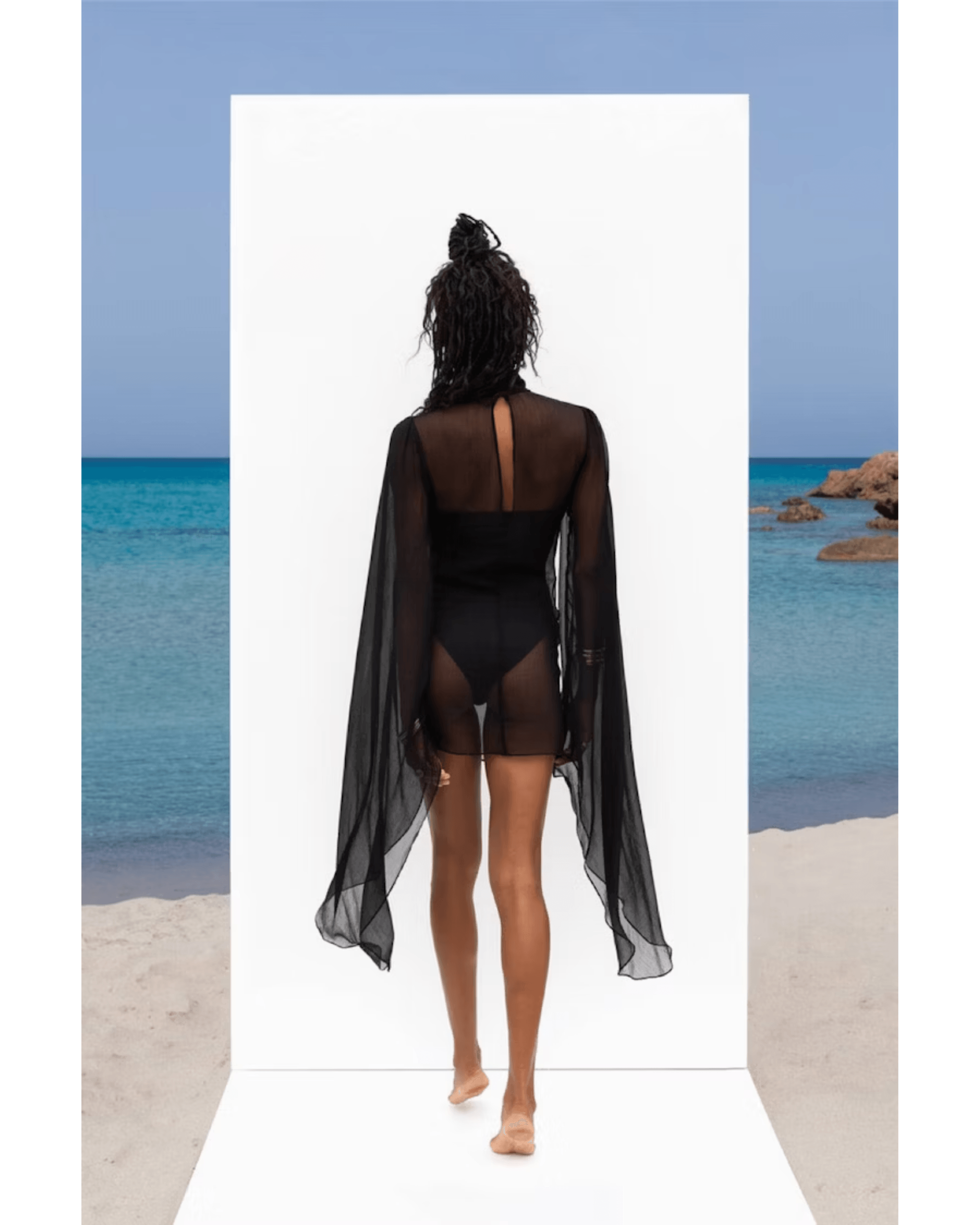 Black sheer mesh maxi dress with flowing cape sleeves and cutout back detail, worn by model at beach — Rat & Boa | Endless UAE