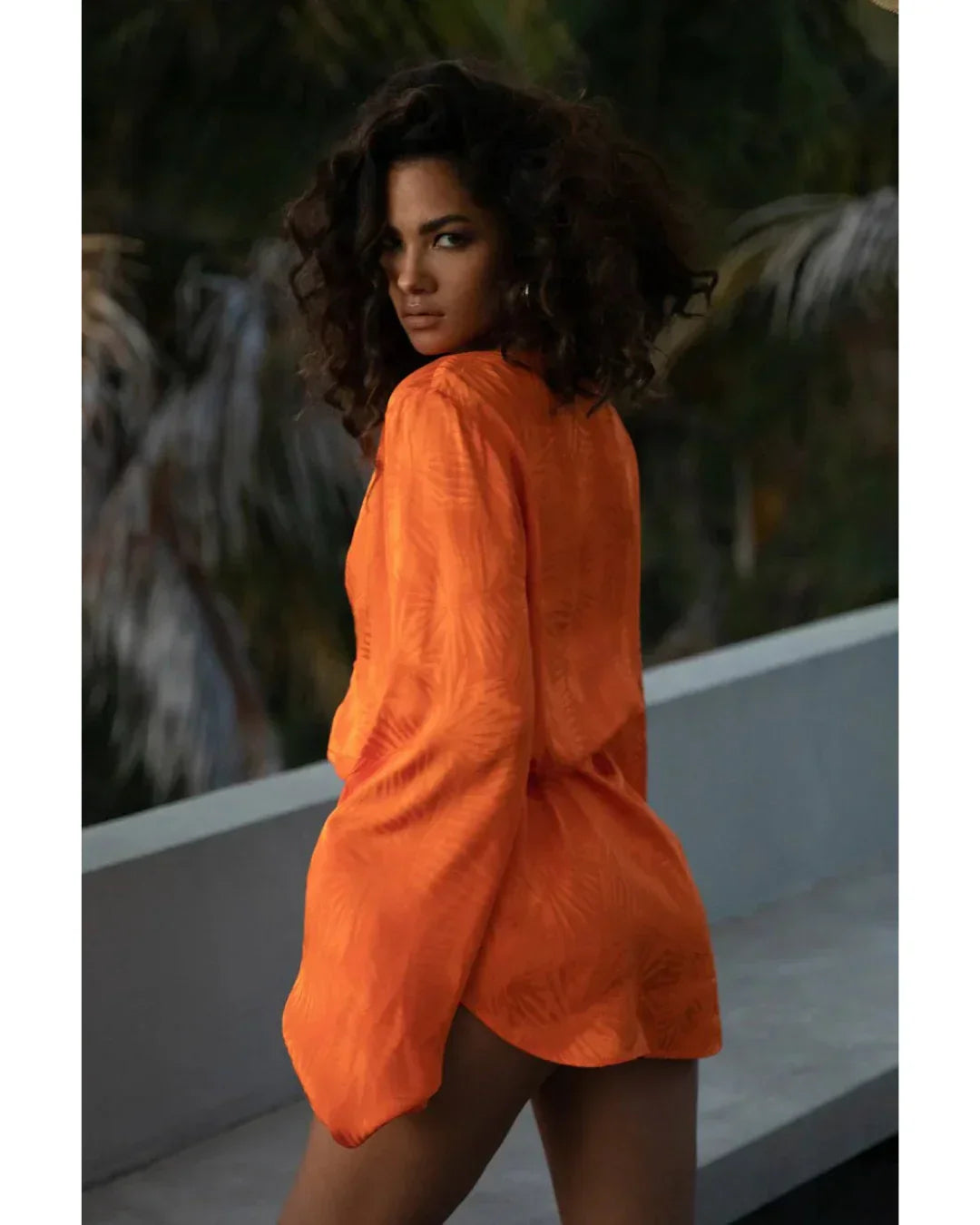 Woman wearing vibrant orange long-sleeve mini dress with textured fabric, shown from behind in tropical setting — Rat & Boa | Endless UAE