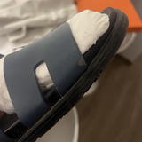 Black leather slide sandals with cutout straps displayed on orange box — Hermès | Endless UAE