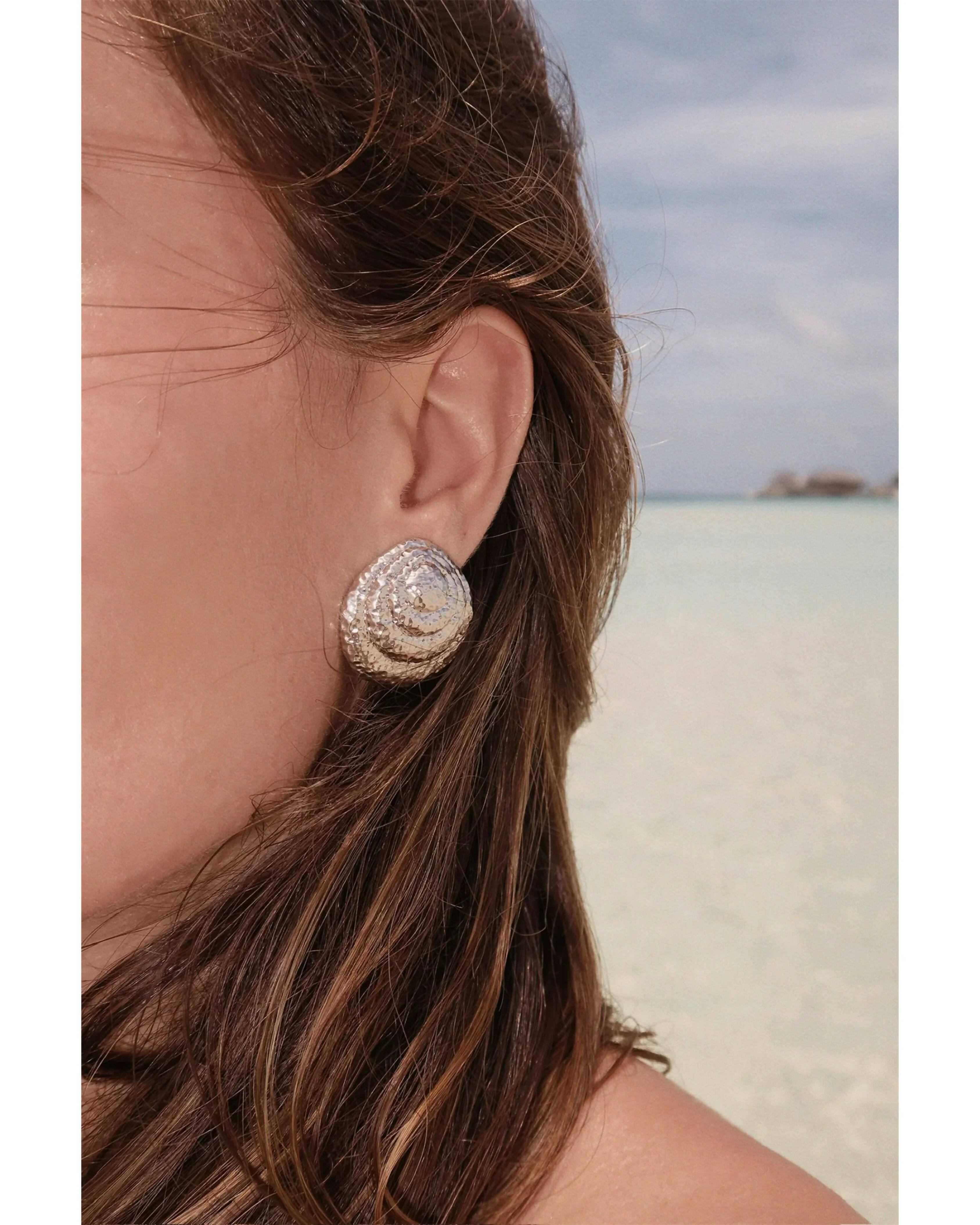 Textured gold seashell dome stud earrings worn on model at beach — Monday Swimwear | Endless UAE