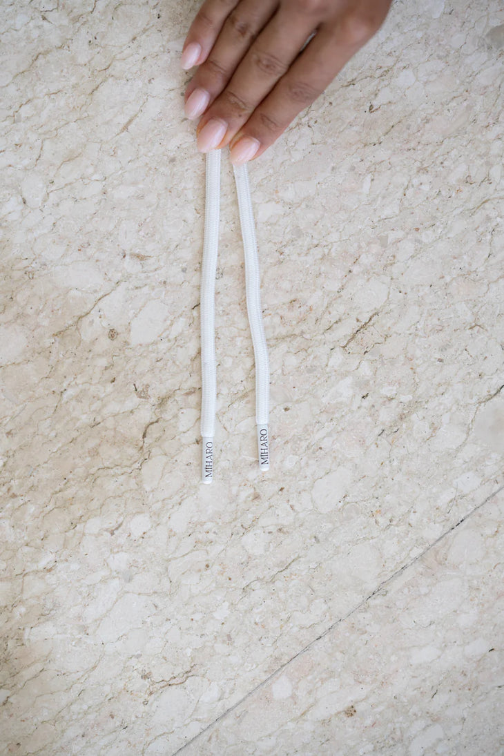 White drawstring cords with Miharo branded metal tips on beige textured surface — Miharo | Endless UAE