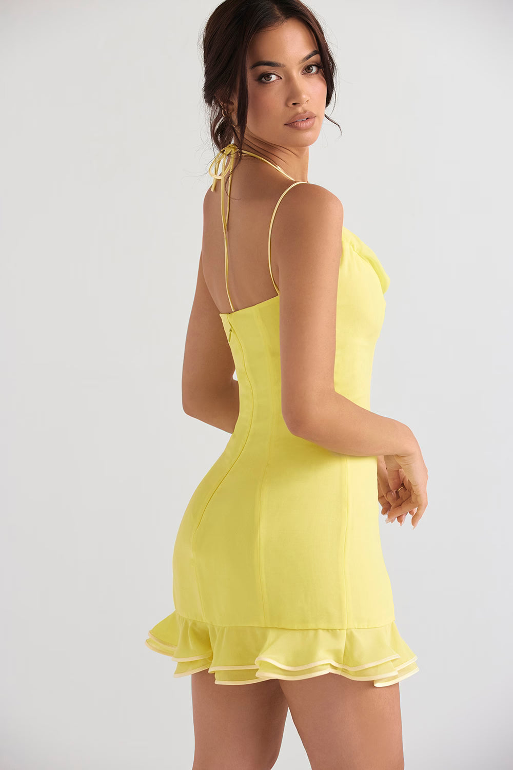 Bright yellow mini dress with spaghetti straps, halter neck tie, and ruffled hem modeled from back — House of CB | Endless UAE