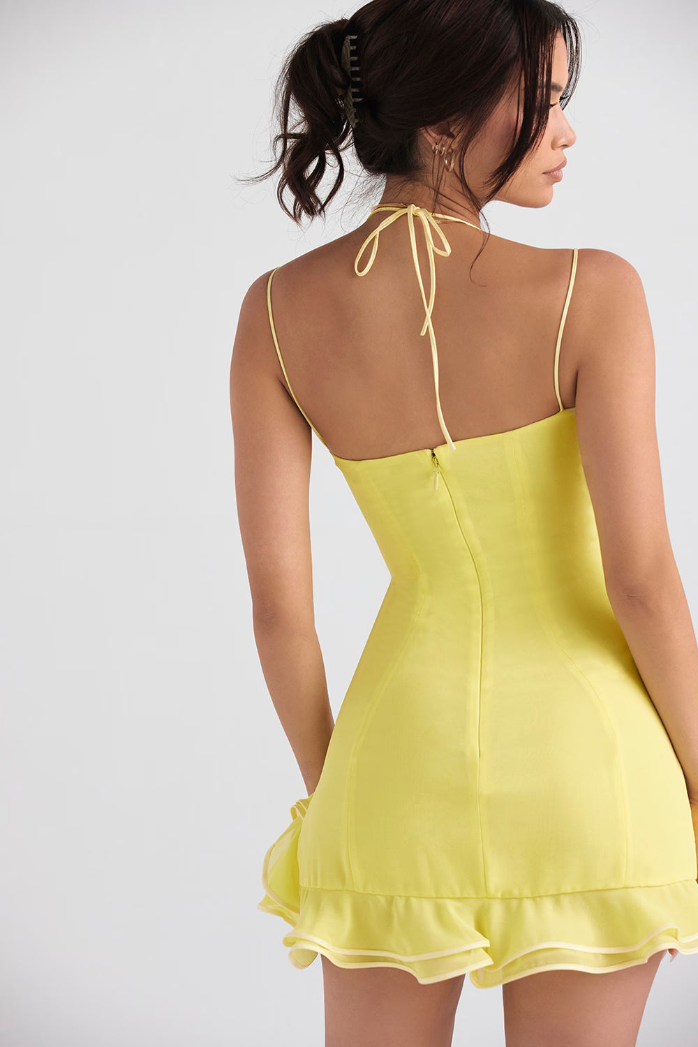 Rear view of woman wearing yellow mini dress with halter neck tie, spaghetti straps, and ruffle hem — House of CB | Endless UAE