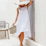 Woman in white sleeveless linen dress with wide-brim straw hat and woven bag, standing in Mediterranean doorway — Magic Linen | Endless UAE