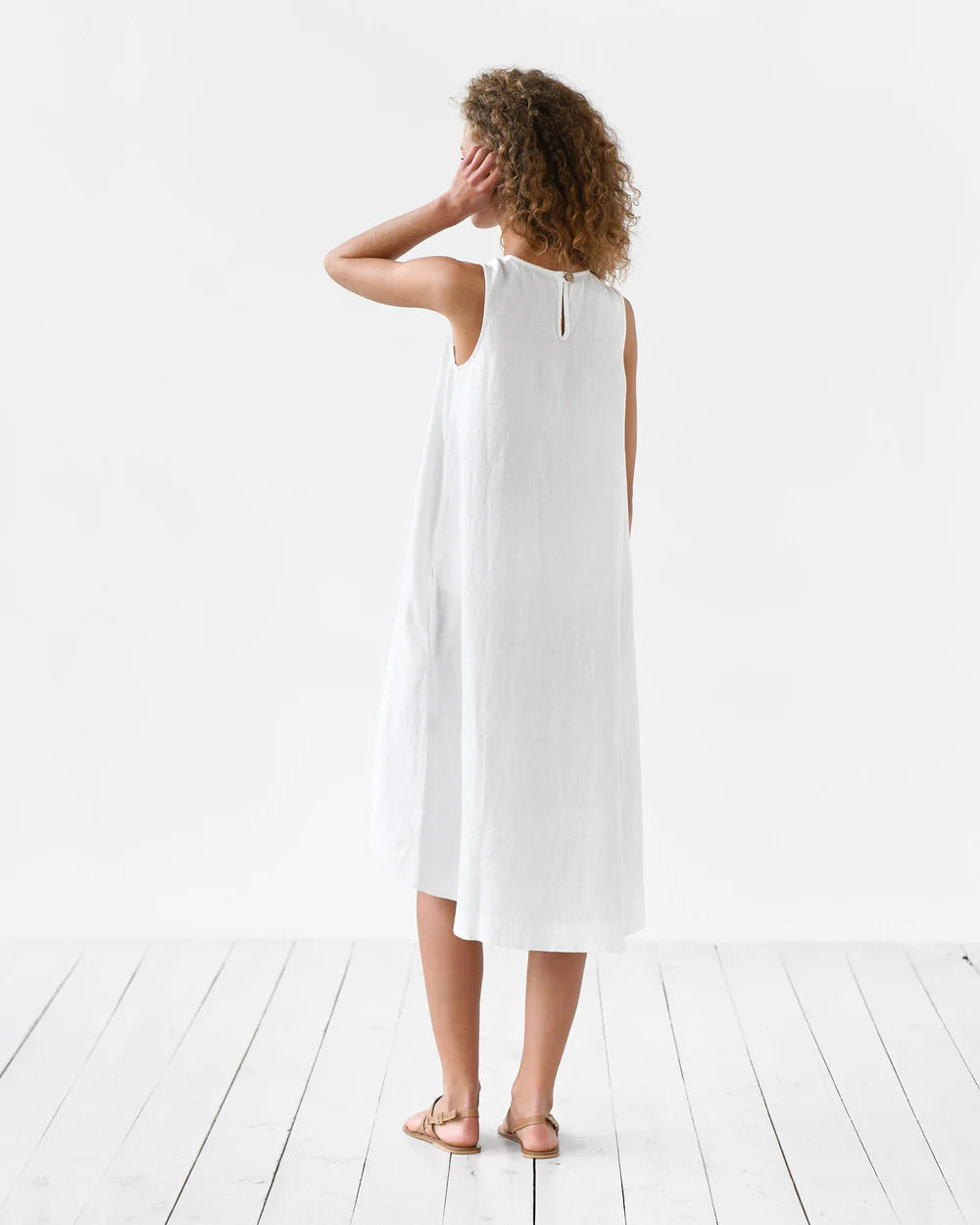 White sleeveless linen midi dress with back zipper, worn by woman with curly hair on white wooden floor — Magic Linen | Endless UAE