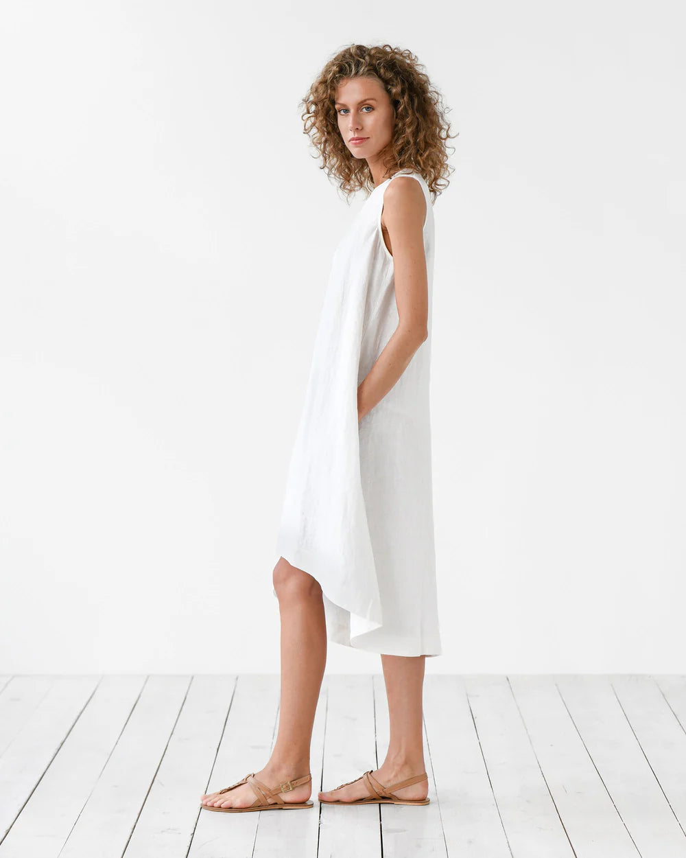 White sleeveless linen midi dress with asymmetric hem and side pockets on woman with curly hair — Magic Linen | Endless UAE