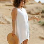 Woman wearing white sleeveless linen dress holding straw hat on beach — Magic Linen | Endless UAE