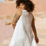 Woman wearing white sleeveless Royal Toscana linen dress outdoors showing floral arm tattoo — Magic Linen | Endless UAE