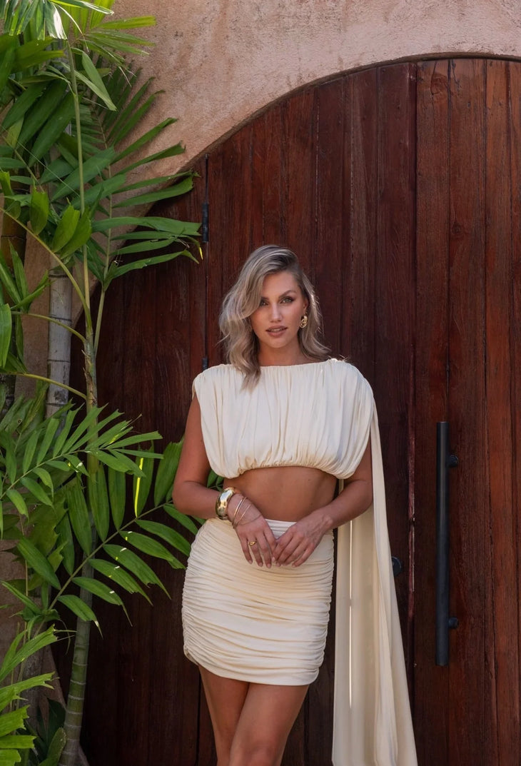 Cream ruched mini skirt worn with matching crop top and flowing cape — Melissa Phair | Endless UAE