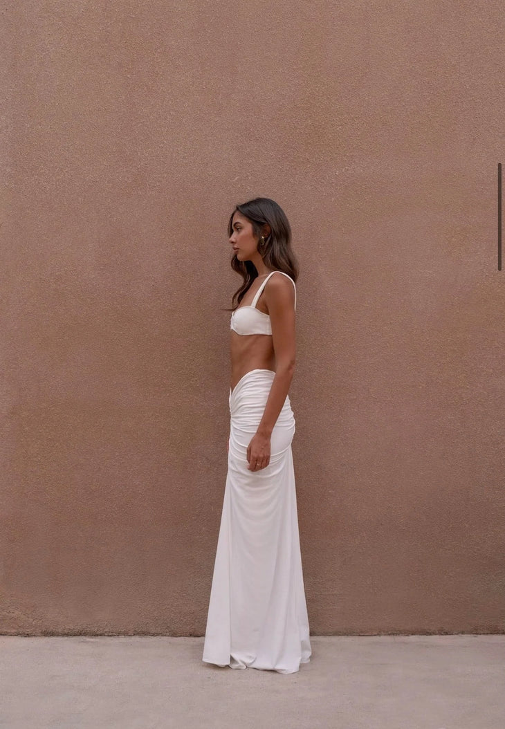 Woman wearing white two-piece set with ruched maxi skirt against beige wall — Melissa Phair | Endless UAE