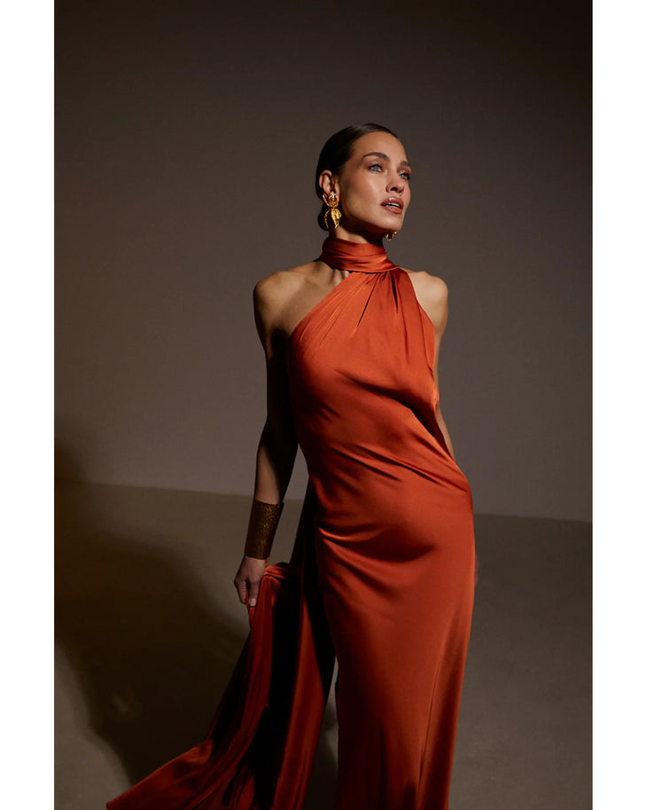 Elegant rust-orange halter neck gown with dramatic draping and train, featuring high neckline and statement gold earrings — Kaoa | Endless UAE