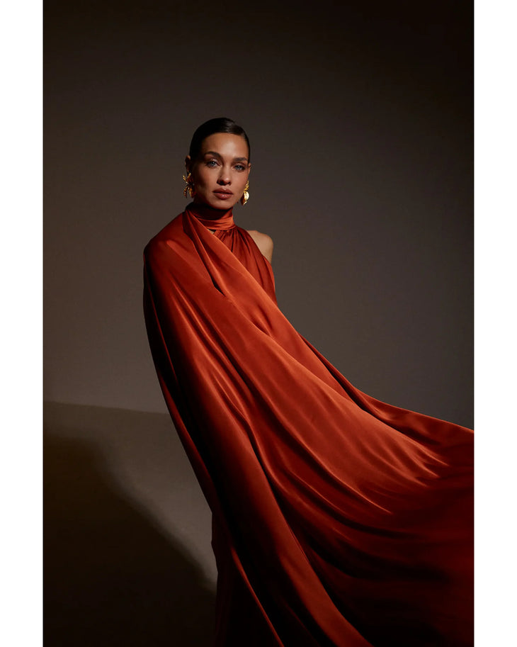 Elegant woman in flowing burnt orange high-neck dress with dramatic draping and sculptural silhouette — Kaoa | Endless UAE