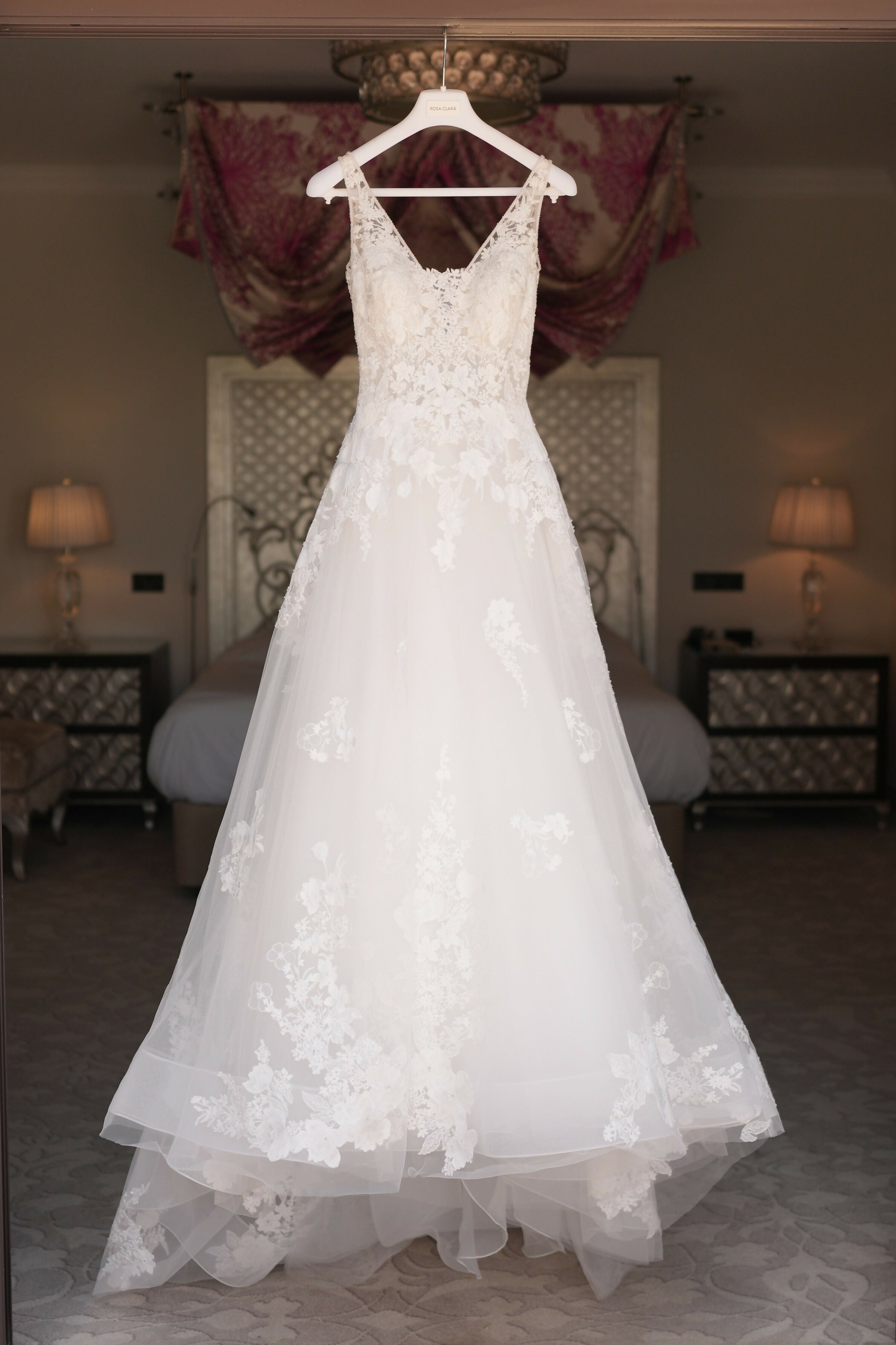 Elegant white lace wedding gown with V-neck and A-line silhouette hanging on display in bedroom — Rosa Clara | Endless UAE