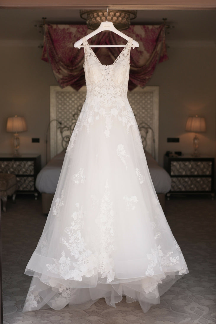 Elegant white lace wedding gown with V-neck and A-line silhouette hanging on display in bedroom — Rosa Clara | Endless UAE