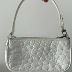 White quilted mini shoulder bag with silver hardware held up against neutral background — By Far | Endless UAE