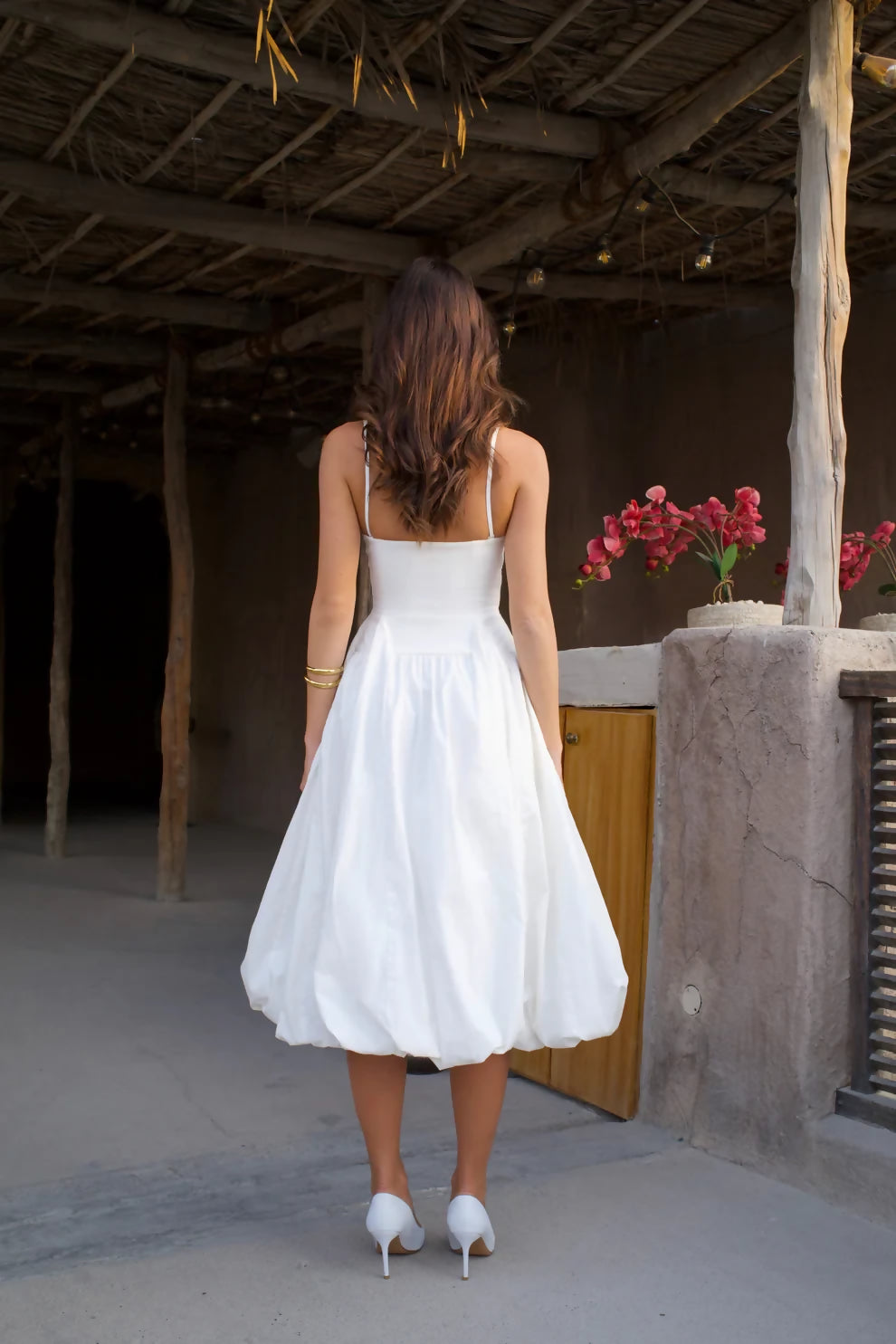 Woman in white strapless midi dress with pleated skirt and white heels against rustic wall — Cleopatress | Endless UAE