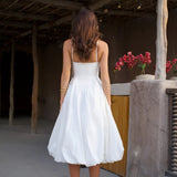 Woman in white strapless midi dress with pleated skirt and white heels against rustic wall — Cleopatress | Endless UAE